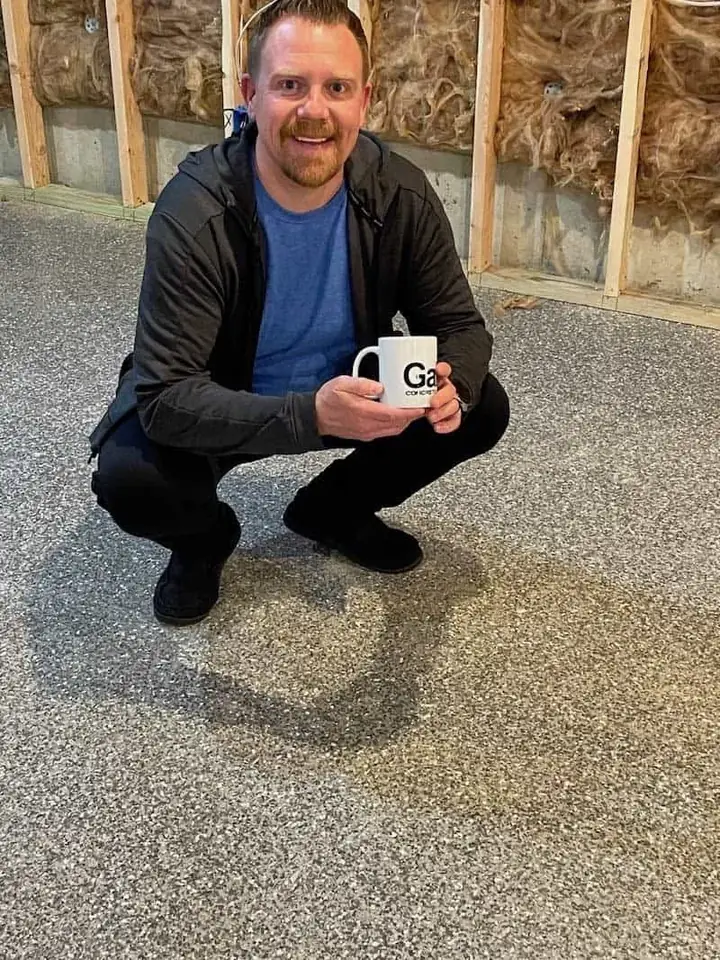 Homeowner crouching on a new flake garage floor holding a Galaxy mug.