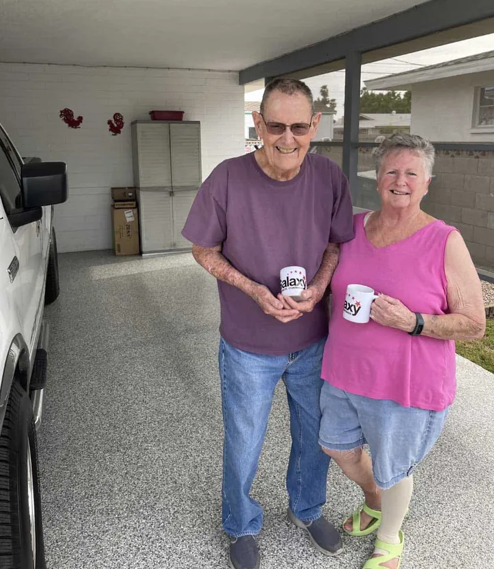 Couple standing in their garage on a new flake floor, each holding a Galaxy mug.