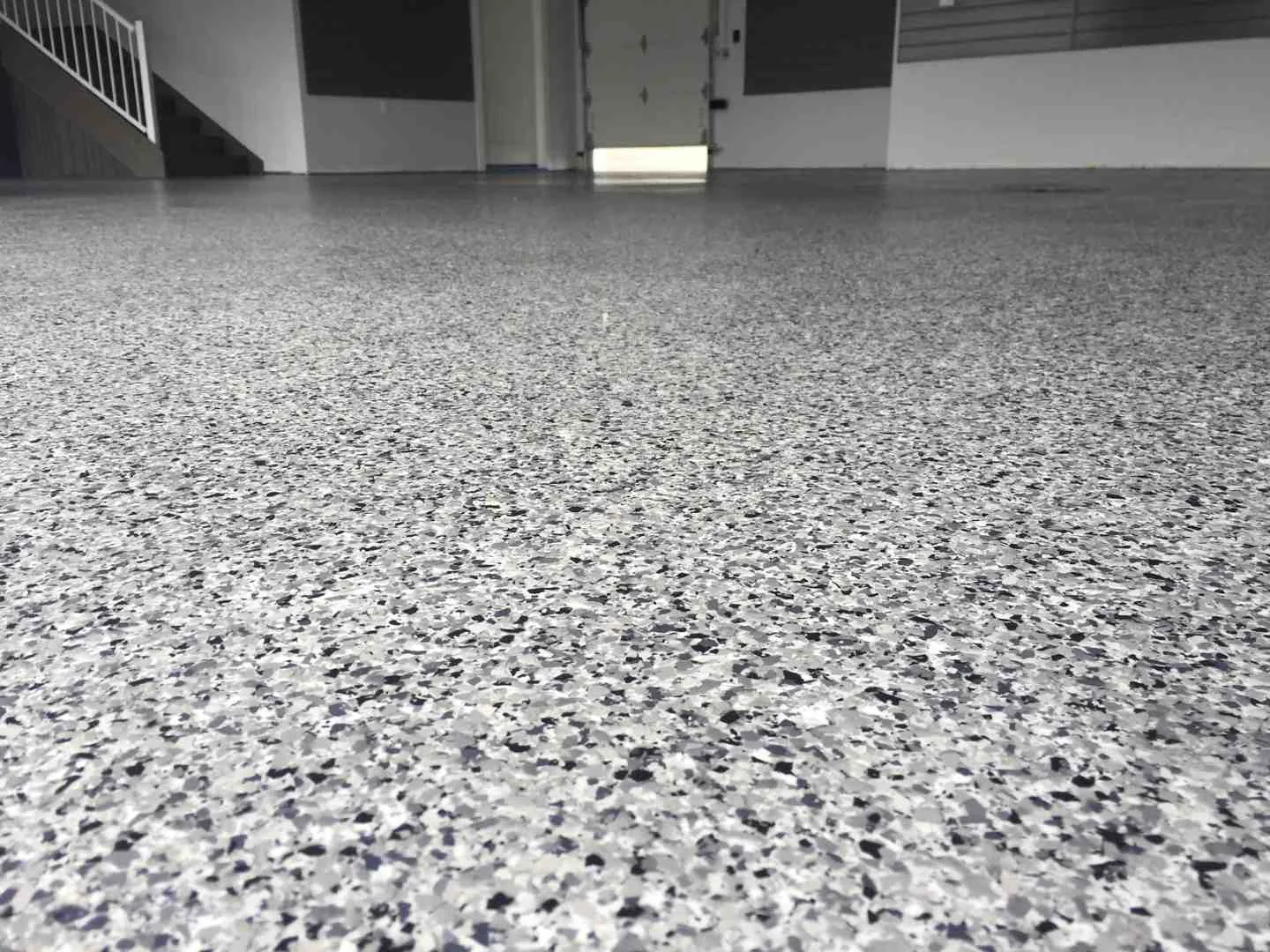 Close-up of a gray and white flake floor coating leading into a garage.